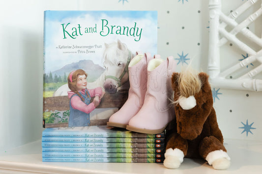Photo of Kat and Brandy books stacked on shelf with boots and stuffed animal toy