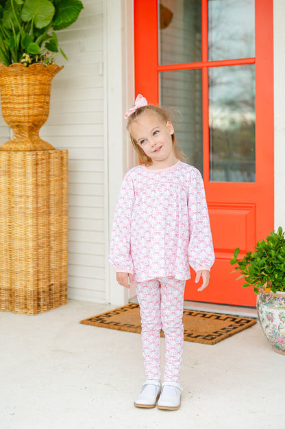 A little girl wearing the Pink Bow Pima Dress with a beautiful pink bow pattern looks absolutely charming and stylish in this soft, elegant outfit.