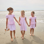 Three young girls in matching pink dresses standing on a beach.