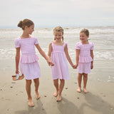 Three young girls in matching pink dresses standing on a beach.