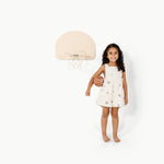 Child in a white dress holding a basketball next to a small basketball hoop on a white background
