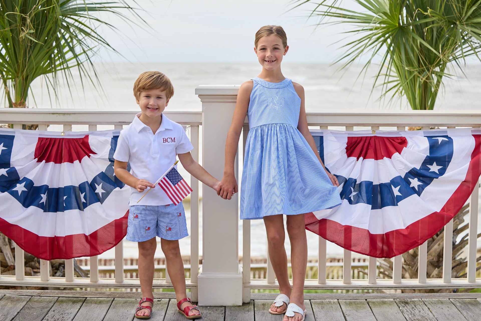 Siblings holding hands on beachfront house deck wearing summer holiday clothing