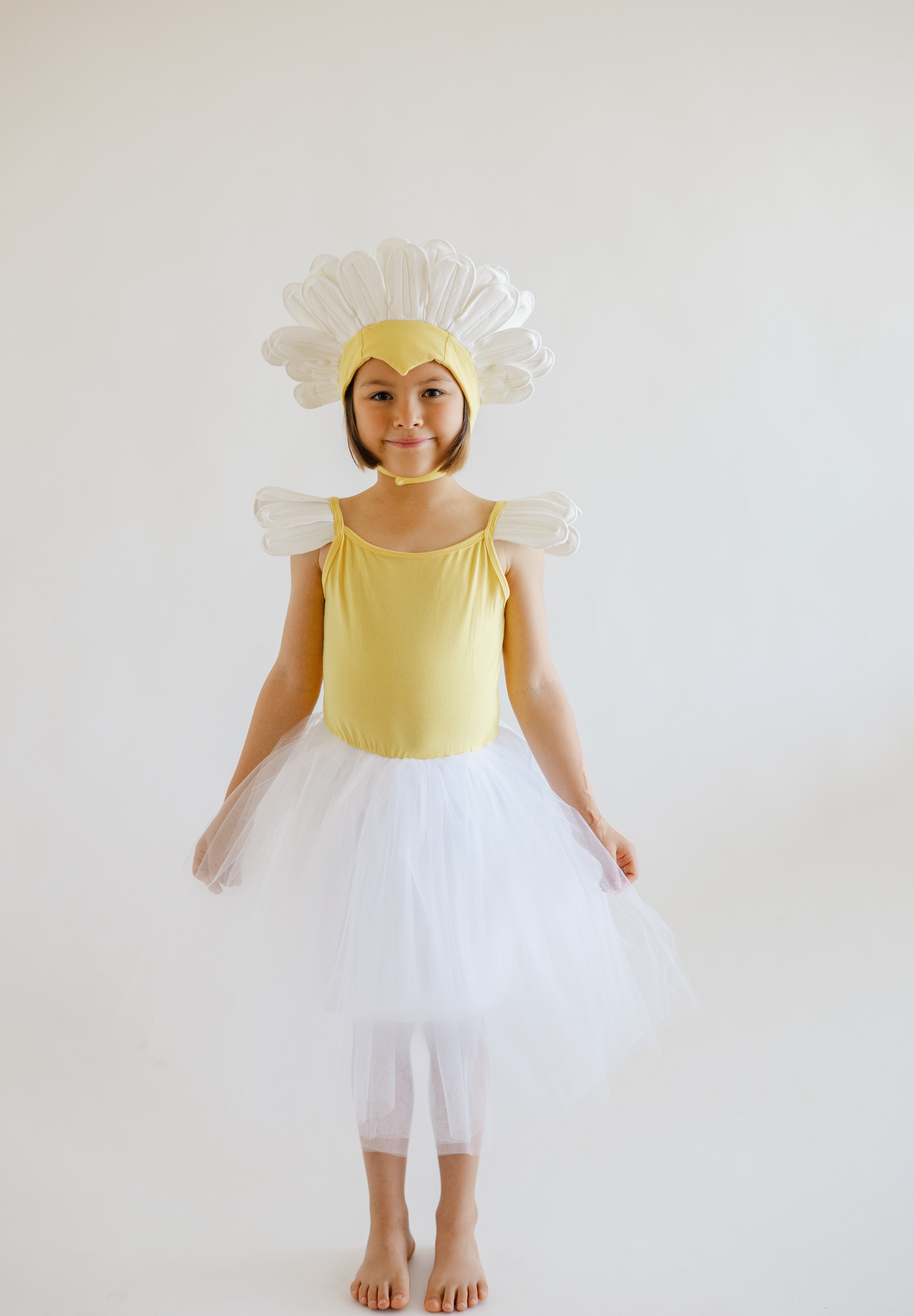 Child in a yellow dress with flower headband and white skirt on a plain background