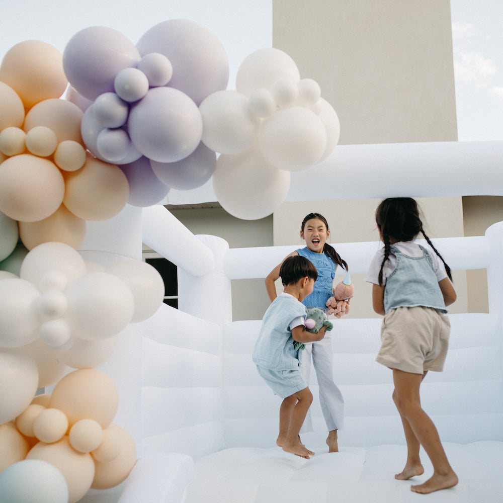 Children playing in a bouncy castle with a colorful balloon arch in the foreground.