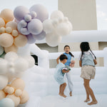 Children playing in a bouncy castle with a colorful balloon arch in the foreground.