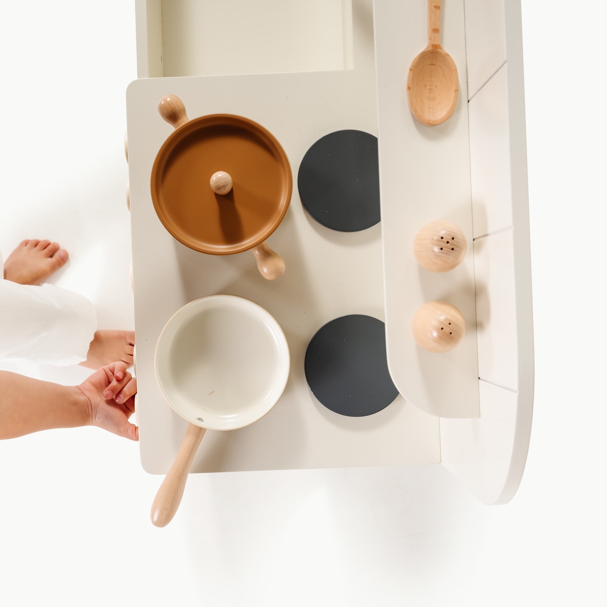 Children's play kitchen set with pots, pans, and lids on a white surface.