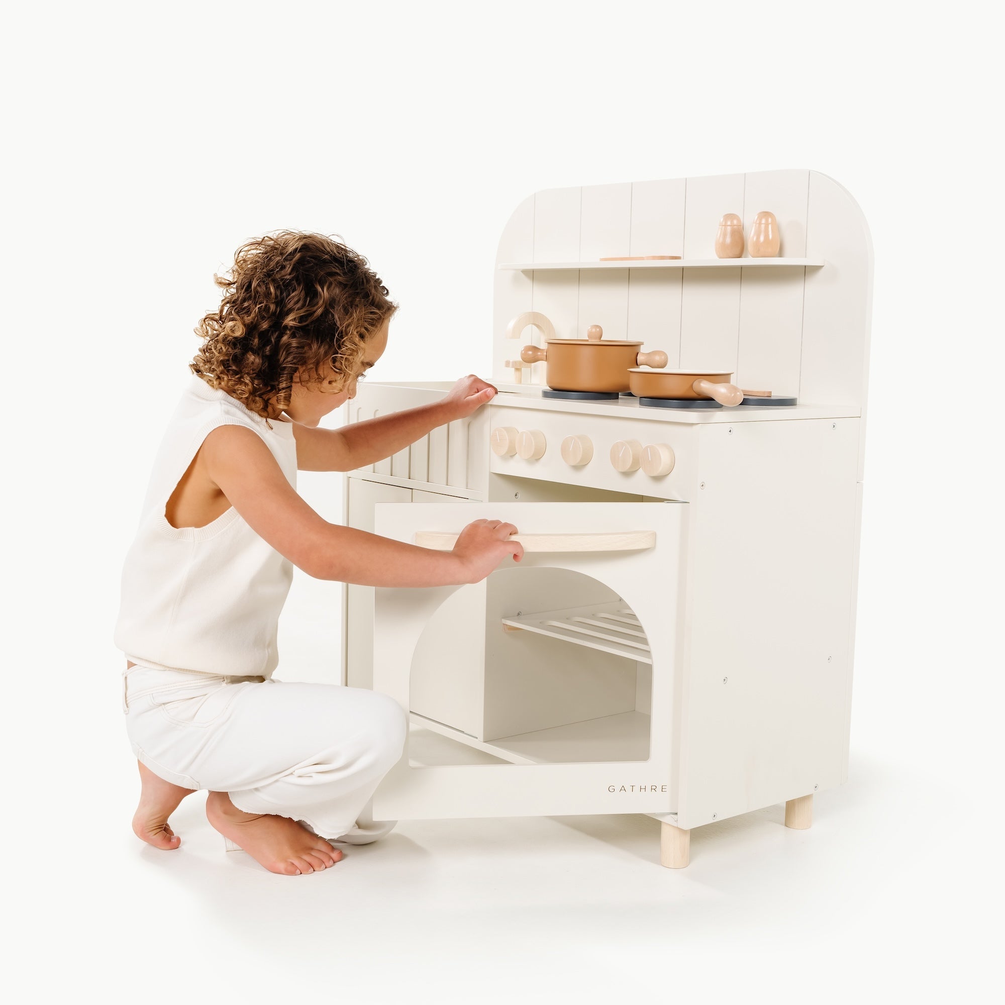 Child playing with a white toy kitchen set on a white background