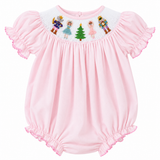 A pink baby romper with short flutter sleeves, elasticized ruffled hem and cuffs, and a white embroidered yoke featuring nutcracker figures, a princess, and a Christmas tree.