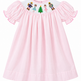 A light pink baby dress with short ruffled sleeves and a white smocked yoke featuring embroidered cartoon characters and a green Christmas tree.