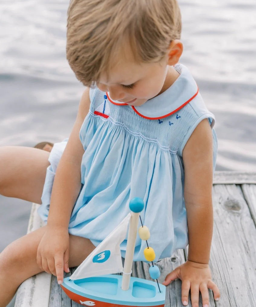 Child playing with a toy sailboat on a wooden dock by water.