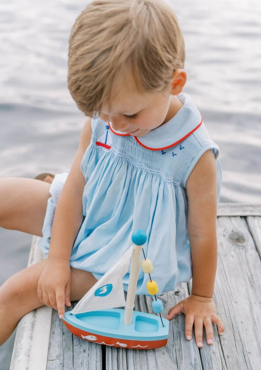 Child playing with a toy sailboat on a wooden dock by water.