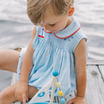 Child playing with a toy sailboat on a wooden dock by water.