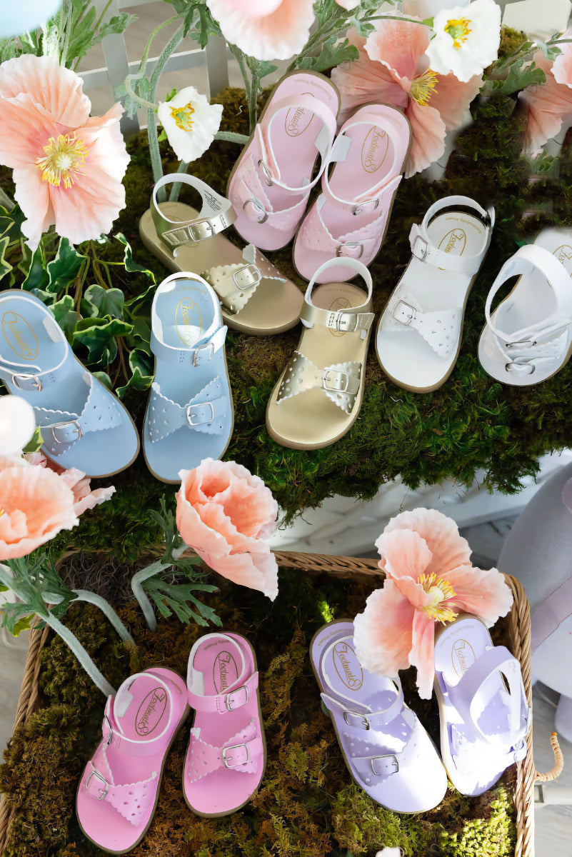 Colorful children's sandals displayed among flowers on a green surface