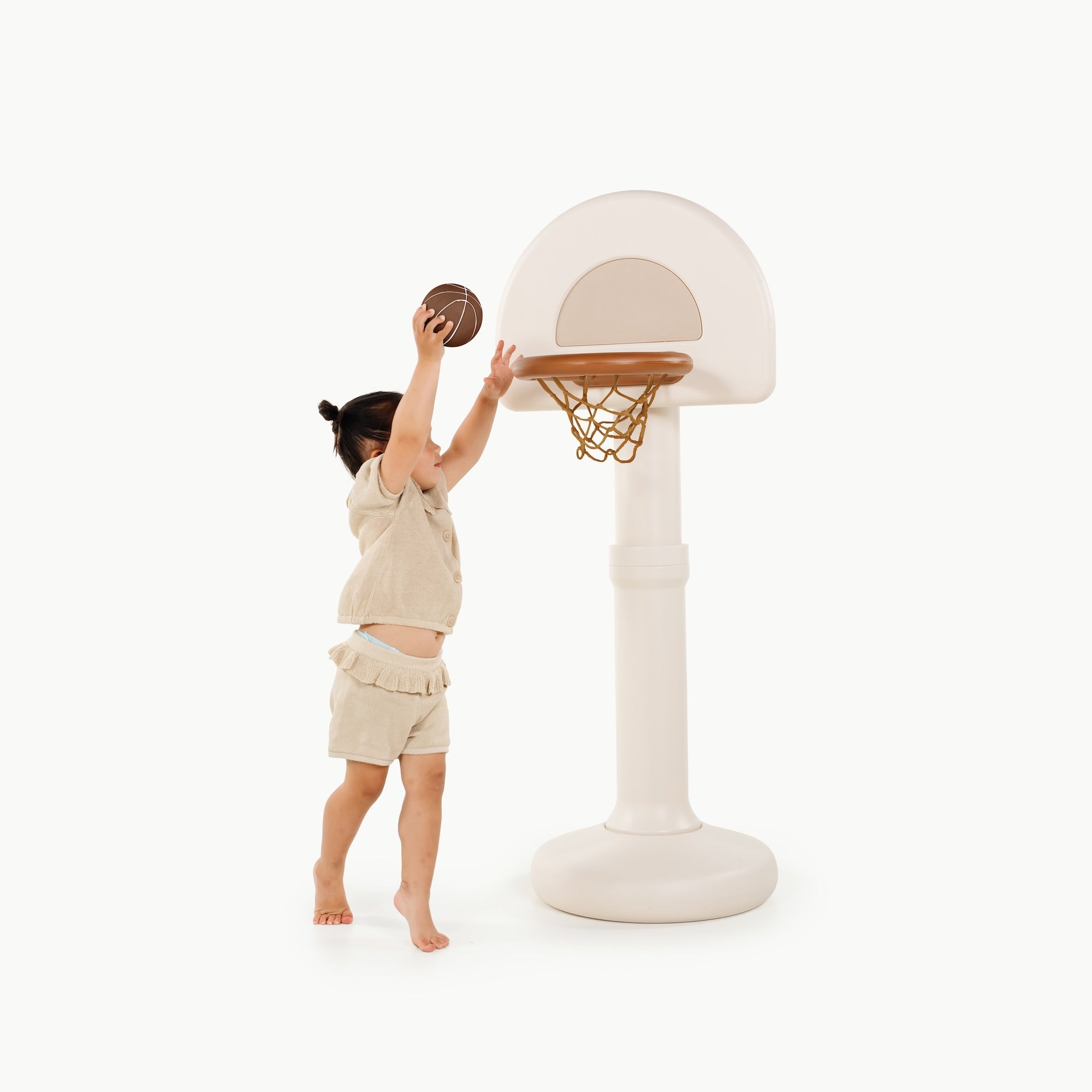 Child playing with a beige basketball hoop and ball on a white background