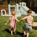Two children holding hands in front of an inflatable playground structure on a grassy area.