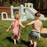 Two children holding hands in front of an inflatable playground structure on a grassy area.