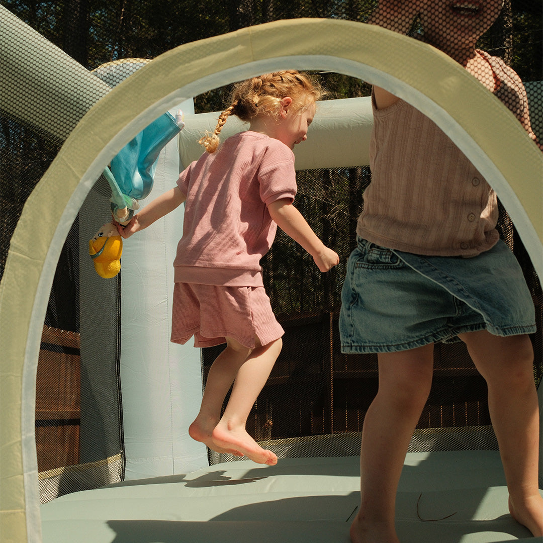 Two children playing on a playground structure with a focus on a young girl in pink.