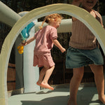 Two children playing on a playground structure with a focus on a young girl in pink.