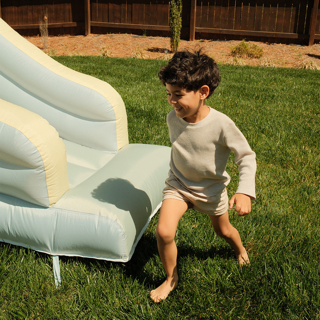 Child playing on a grassy area with an inflatable slide.
