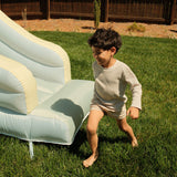 Child playing on a grassy area with an inflatable slide.