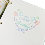 Notebook with decorative cover featuring balloons and text on a white background