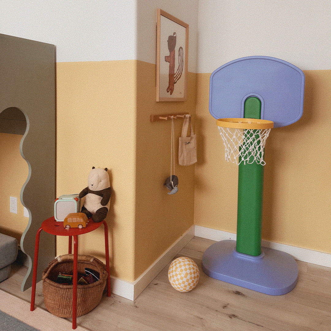 Children's playroom with a colorful basketball hoop, toys, and a teddy bear.