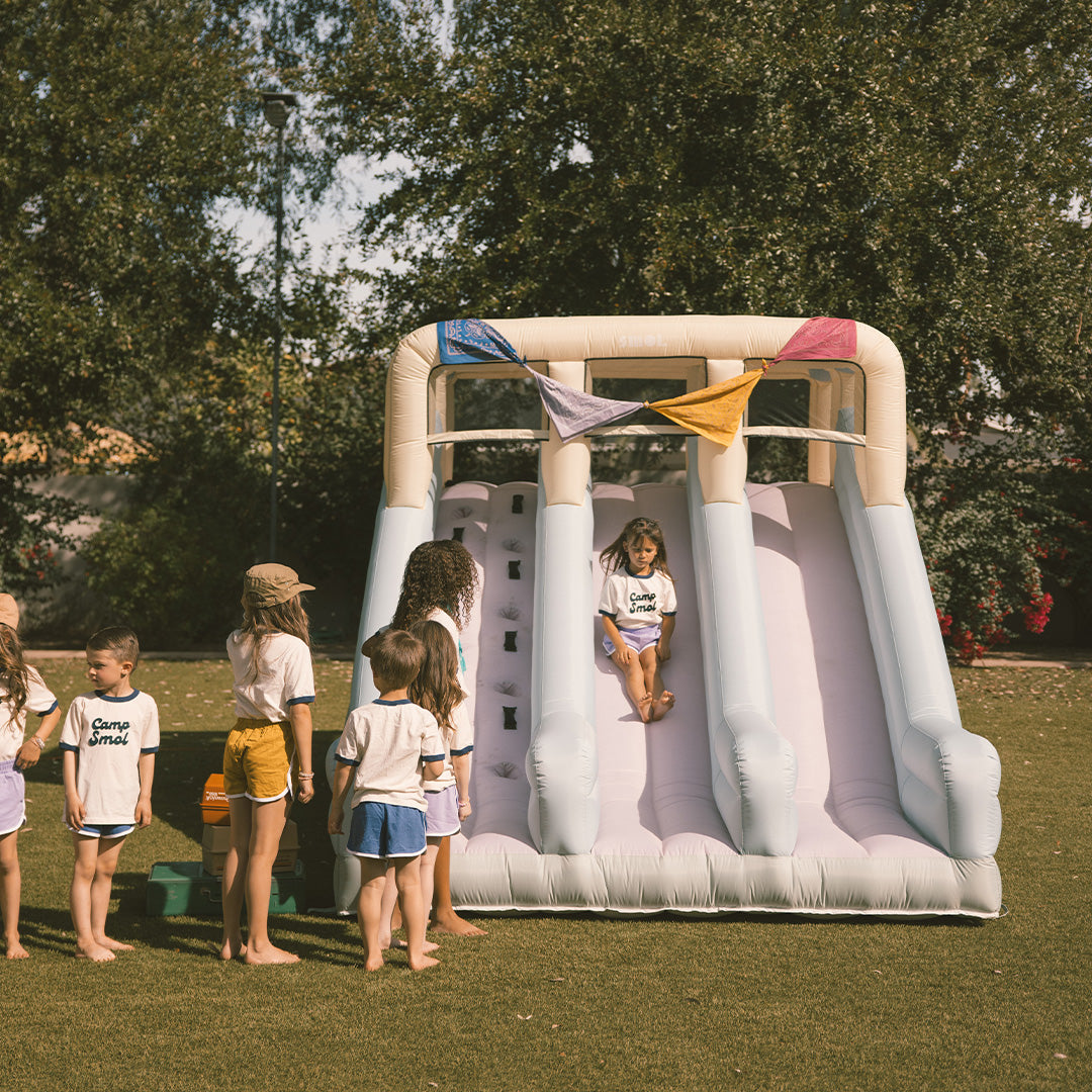 Children playing on an inflatable slide in a park with trees in the background
