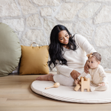 Woman and baby playing on a wooden floor with toys and pillows.