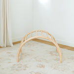 Beige play arch on a light wooden floor with a white wall background