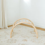 Beige play arch on a light wooden floor with a white wall background