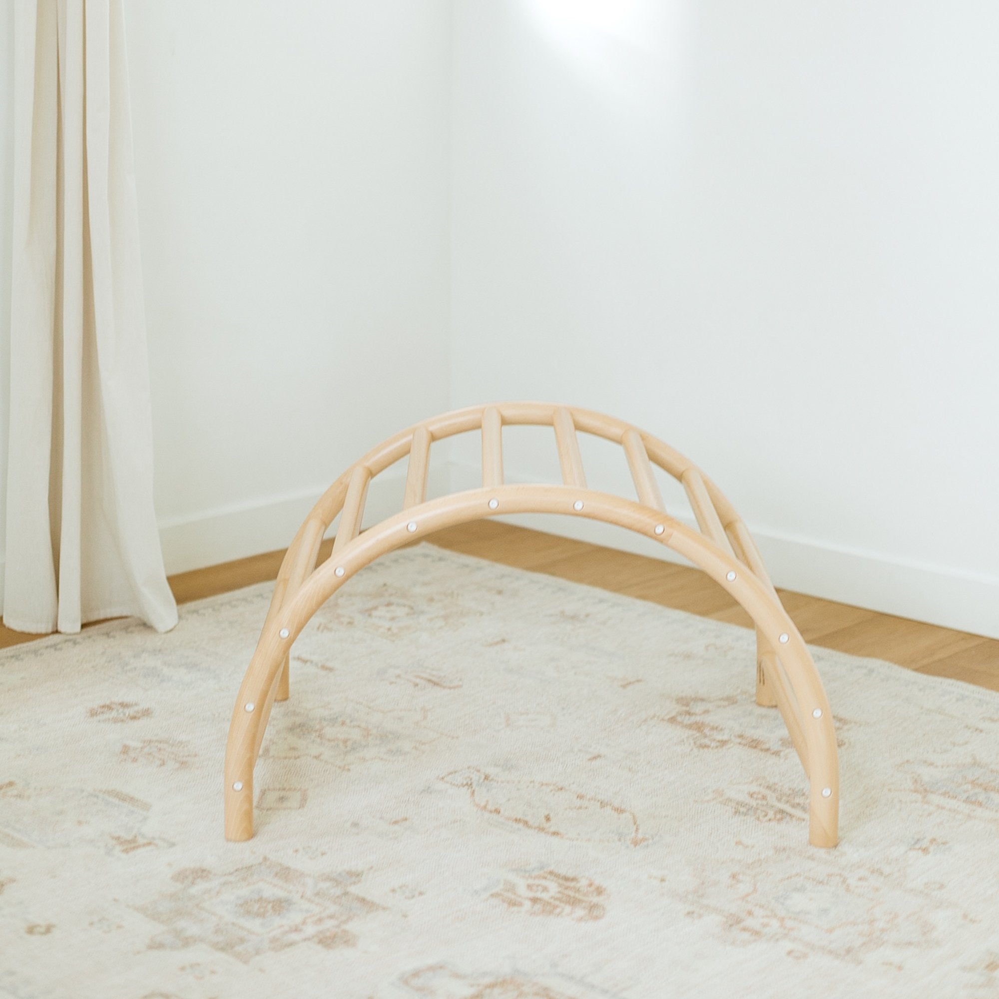 Beige play arch on a light wooden floor with a white wall background