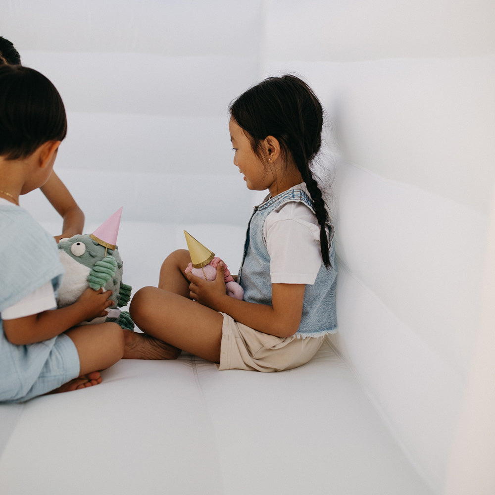 Two children sitting on a white surface with plush toys.