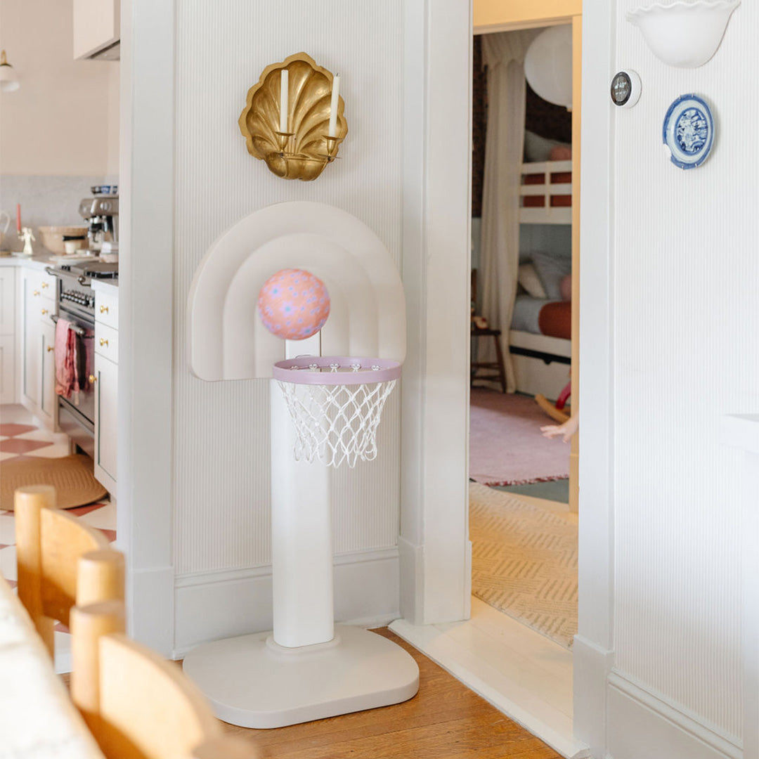 Children's basketball hoop with a ball in a room with a kitchen and bedroom in the background.