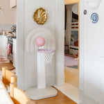 Children's basketball hoop with a ball in a room with a kitchen and bedroom in the background.
