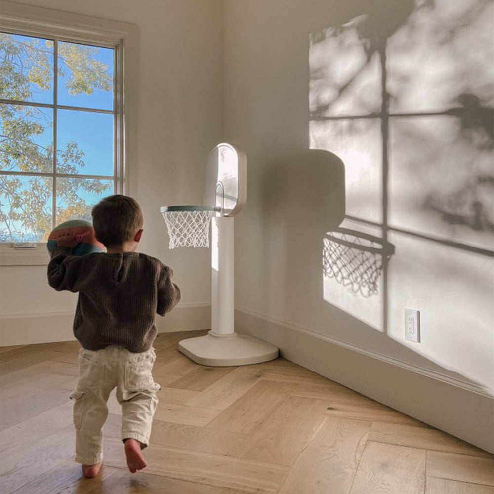 Child playing with a basketball hoop in a room with a large window.