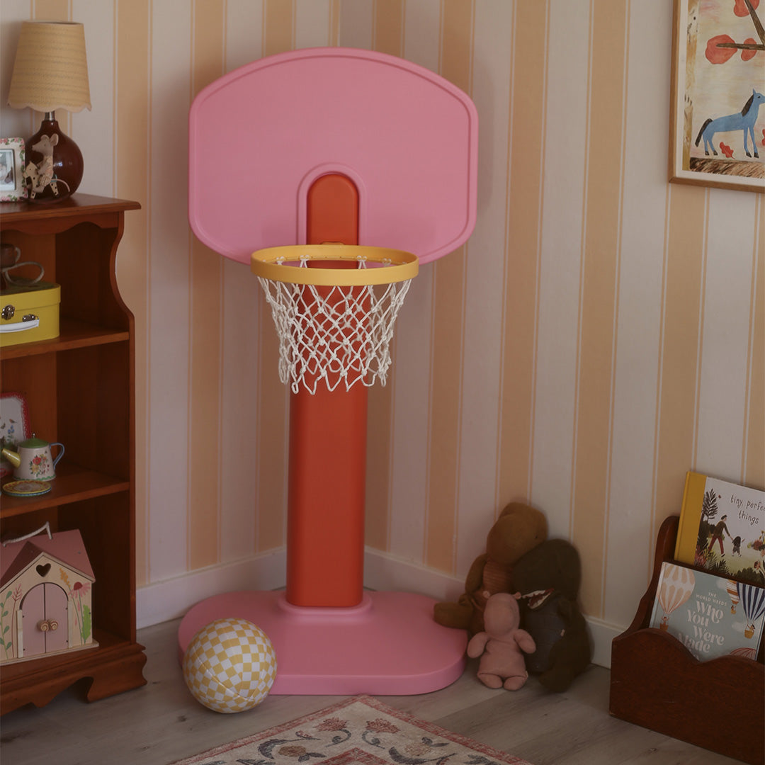 Children's pink basketball hoop in a room with striped wallpaper and toys.