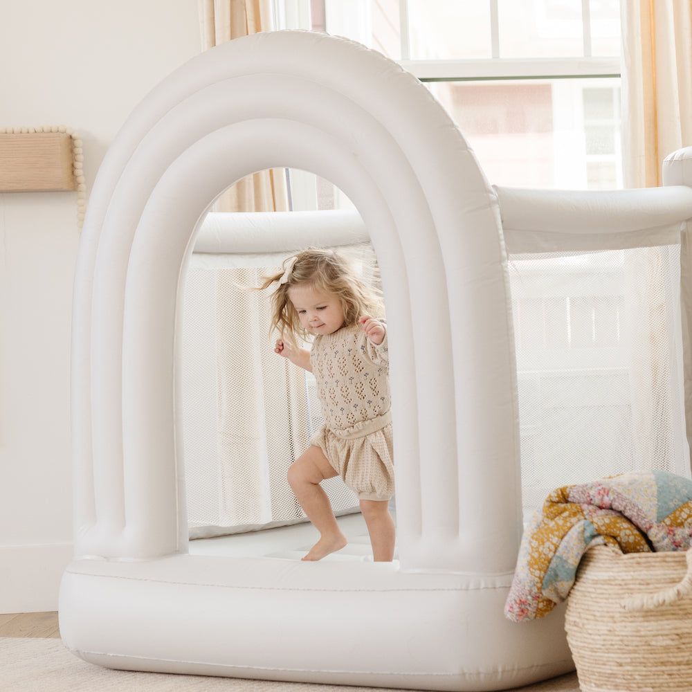 Child playing inside a white inflatable archway in a bright room.