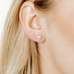 Close-up of a person wearing a stud earring with a purple gemstone.