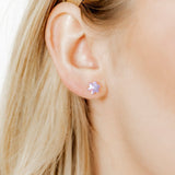 Close-up of a person wearing a stud earring with a purple gemstone.