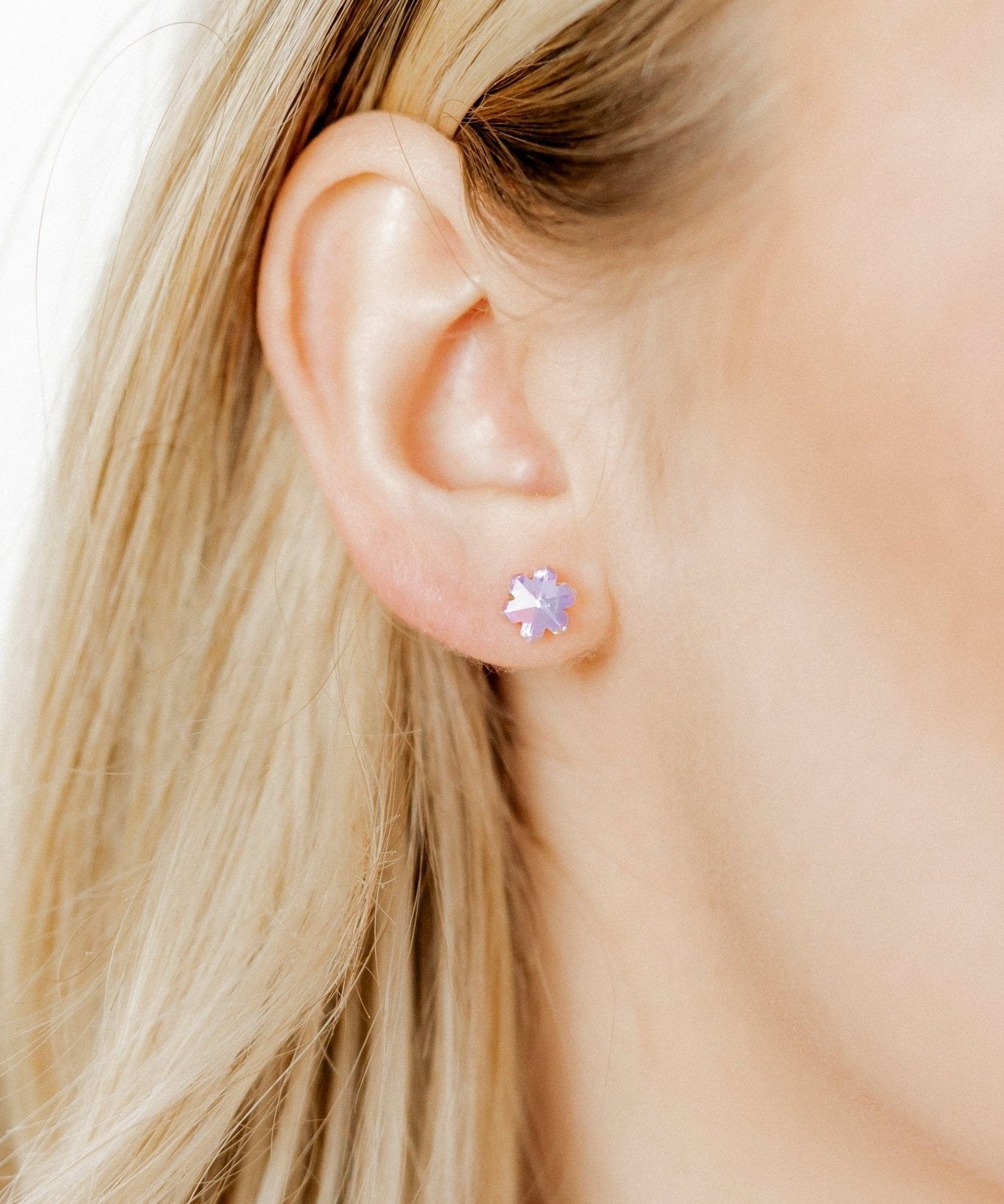 Close-up of a person wearing a stud earring with a purple gemstone.