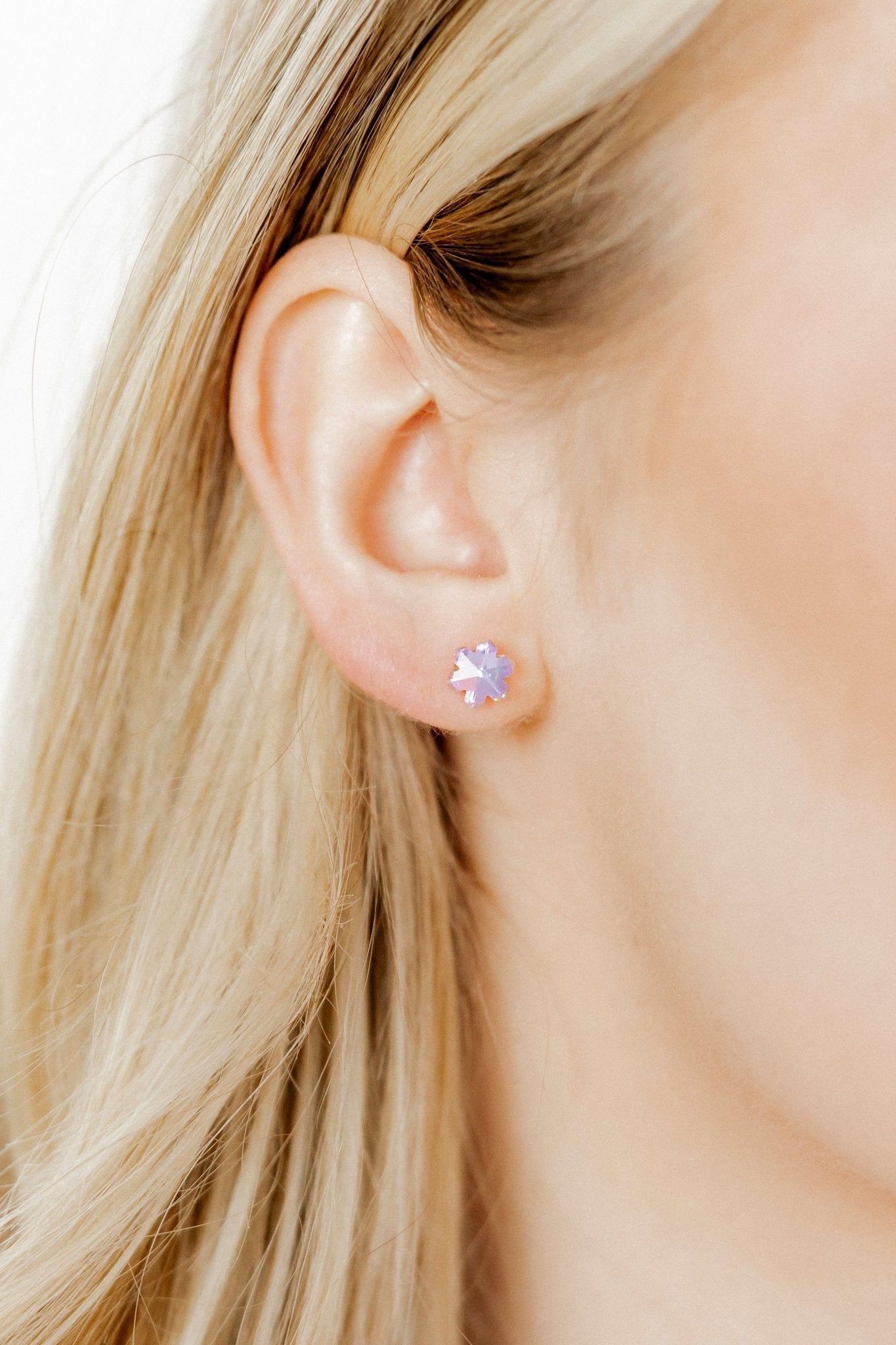 Close-up of a person wearing a stud earring with a purple gemstone.