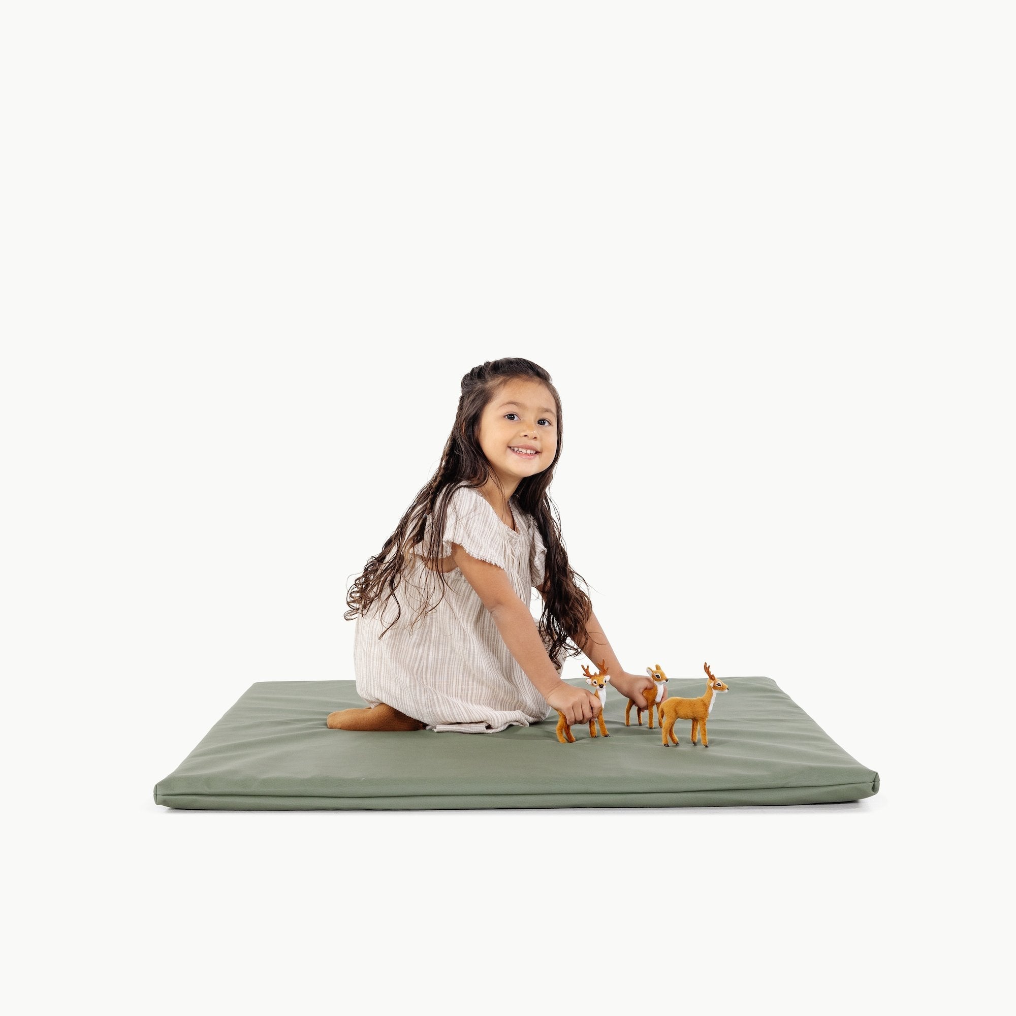 Child playing with toy deer on a green mat against a white background