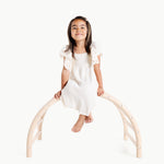 Young girl sitting on a white arch structure against a white background