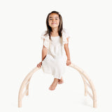 Young girl sitting on a white arch structure against a white background